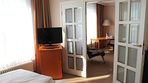 A hotel room with a bed, a desk with a chair, a television, and a door leading to another room.