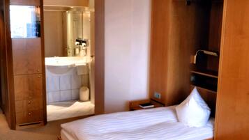 Habitación de hotel con cama, armario de madera, escritorio y baño visible a través de una puerta abierta.