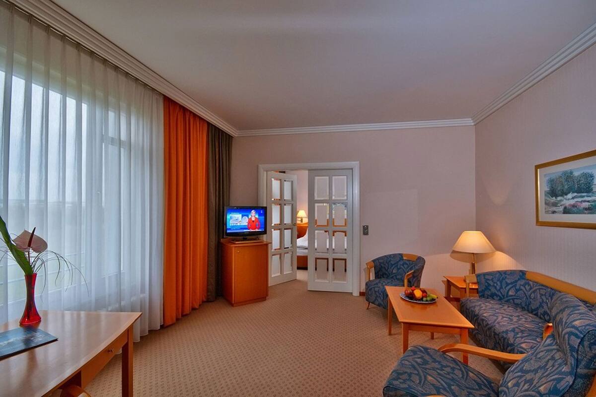 Una habitación de hotel con televisión, un sofá, una mesa con fruta, una lámpara y un cuadro en la pared.