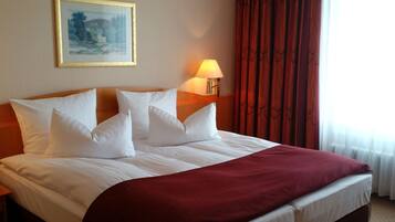 Una cama bien hecha con sábanas blancas y un plaid rojo, una lámpara de noche y un cuadro en la pared.