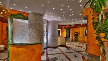 Un vestíbulo de hotel con pisos de baldosas, amplias columnas y una fuente.