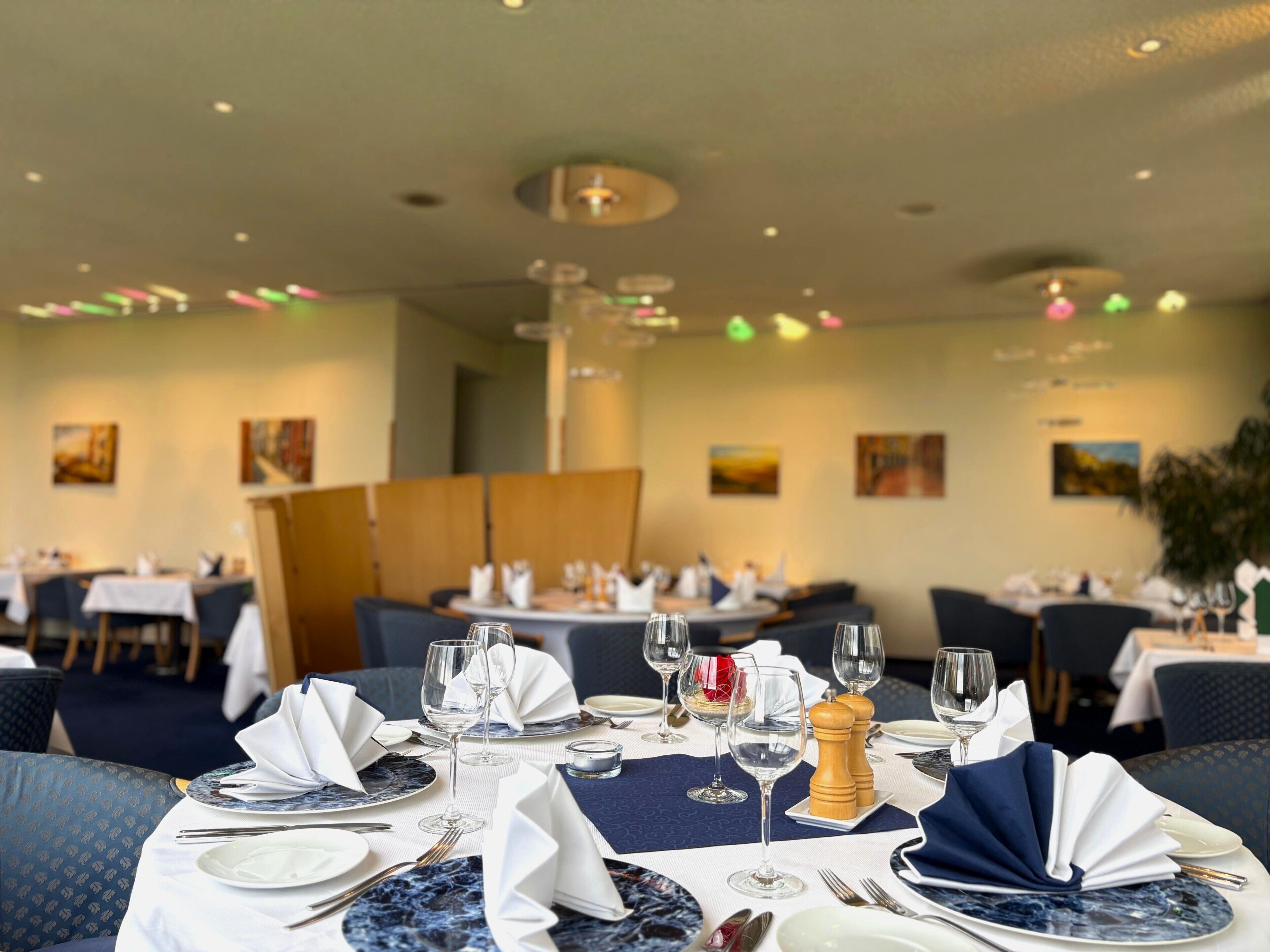 A restaurant with tables set for dining, featuring a marble tablecloth, white napkins, and wine glasses.