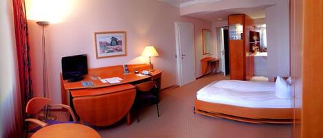 A hotel room with a bed, desk, chair, TV, and a painting on the wall.