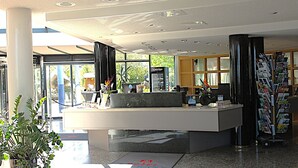 A reception desk with a glass partition, a coffee machine, and a magazine rack.