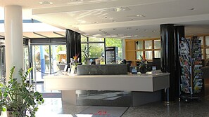 A reception desk with a glass partition, a coffee machine, and a magazine rack.