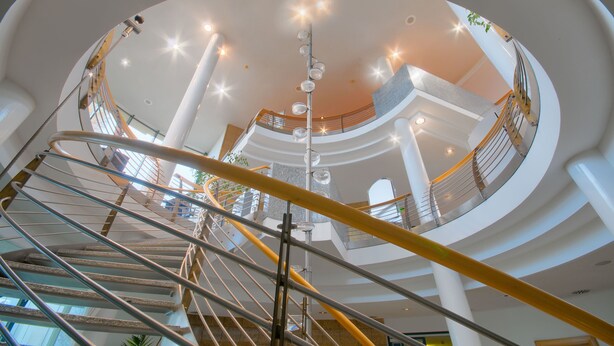 A multi-level atrium with a central spiral staircase, glass railings, and a modern architectural design. - Hotel Meerane (Meerane)
