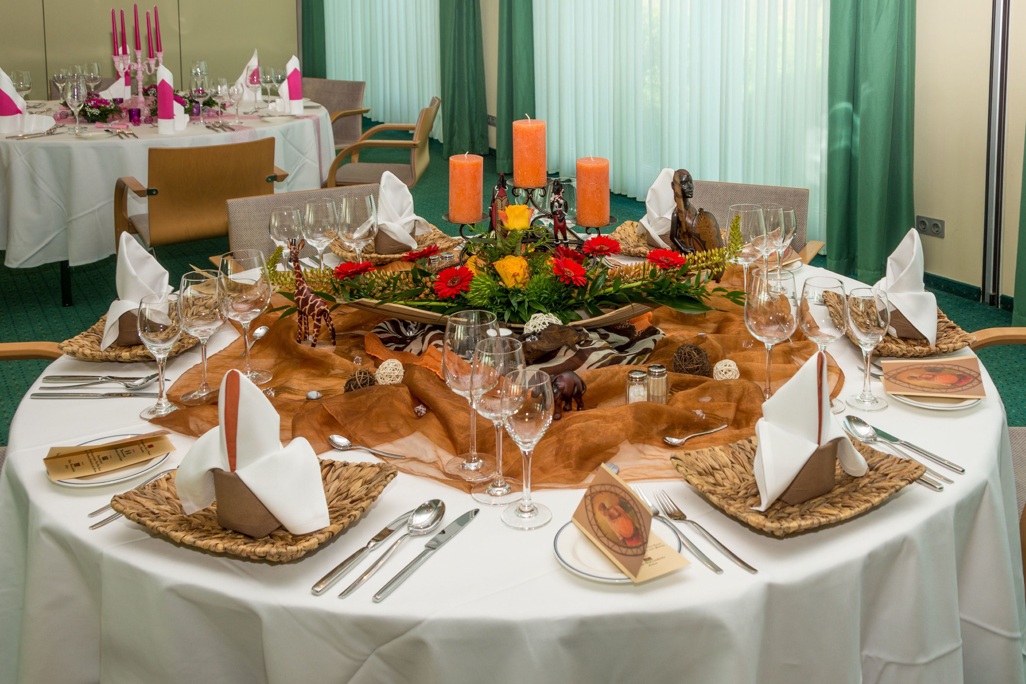 Une table ronde dressée pour un repas formel, agrémentée de bougies, de verres et d’un centre de table.