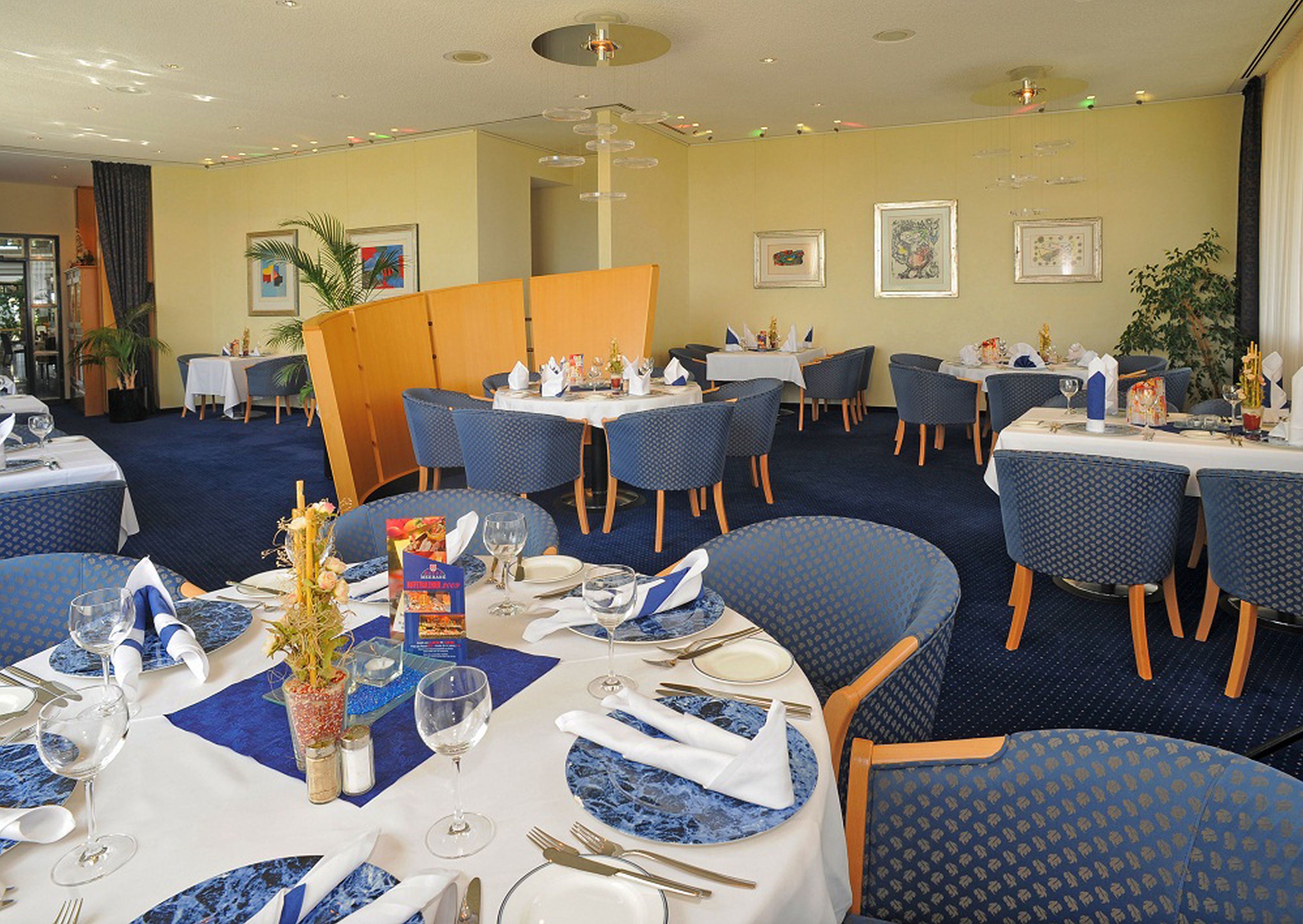 Un restaurante con mesas redondas, sillas tapizadas en azul y suelo alfombrado.
