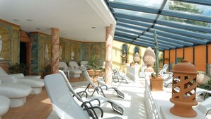 A sunlit indoor patio with white lounge chairs, a glass ceiling, and decorative columns. - Hotel Meerane (Meerane)