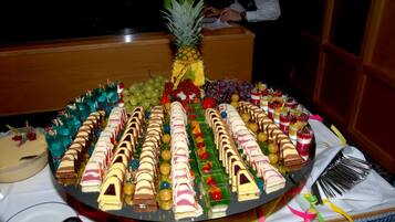 A large, round dessert platter with various types of cakes and pastries, a pineapple, and an assortment of fruits and beverages.
