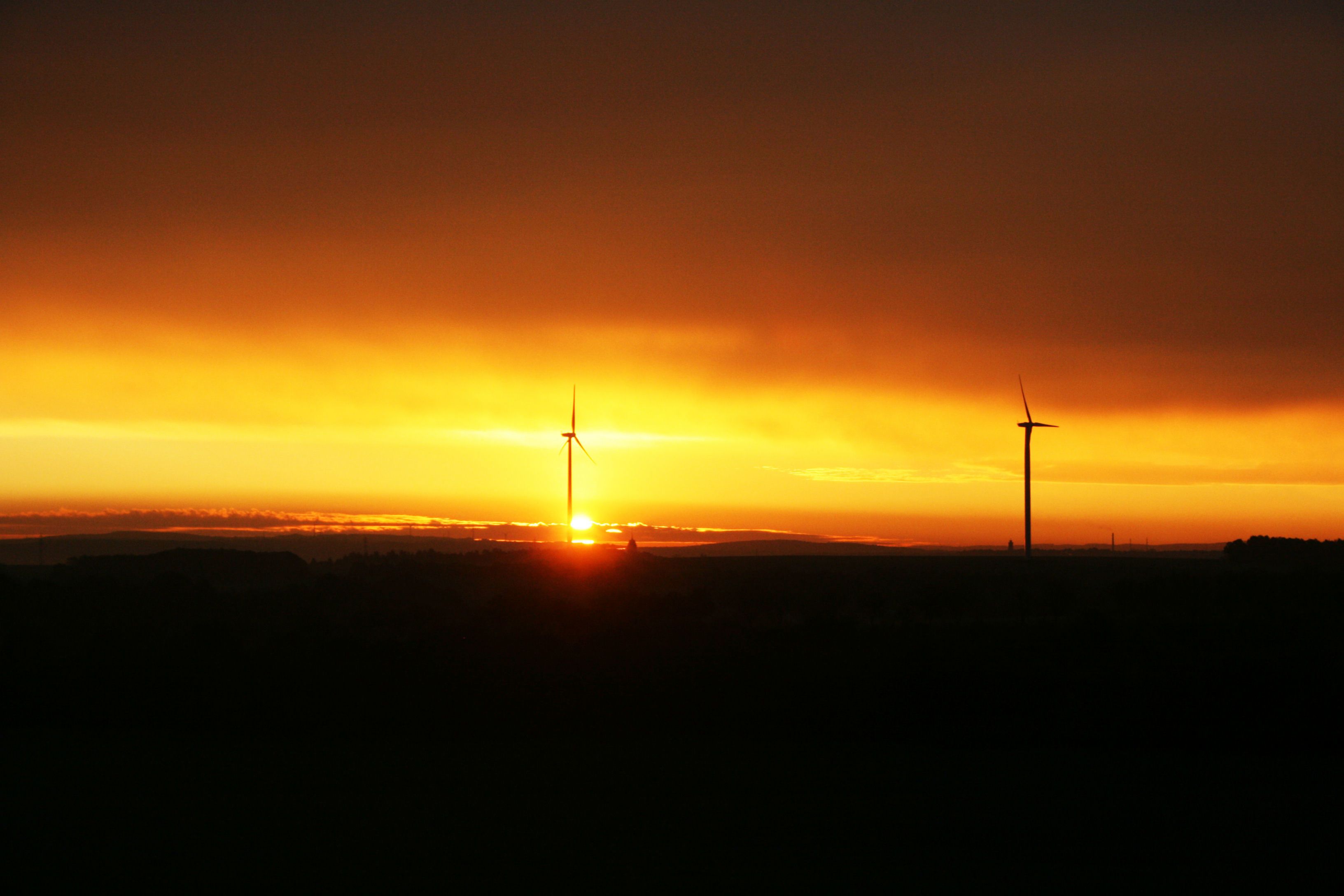 Un coucher de soleil avec deux éoliennes se détachant en silhouette sur un ciel aux couleurs éclatantes.