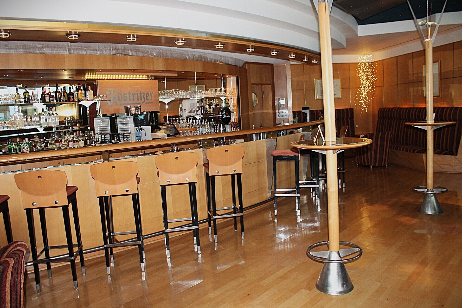 Zona de bar con taburetes, una barra con botellas y una lámpara colgante.