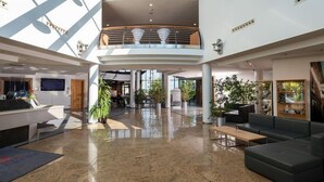 A spacious lobby with a high ceiling, a reception desk, seating areas, and a mezzanine level. - Hotel Meerane (Meerane)