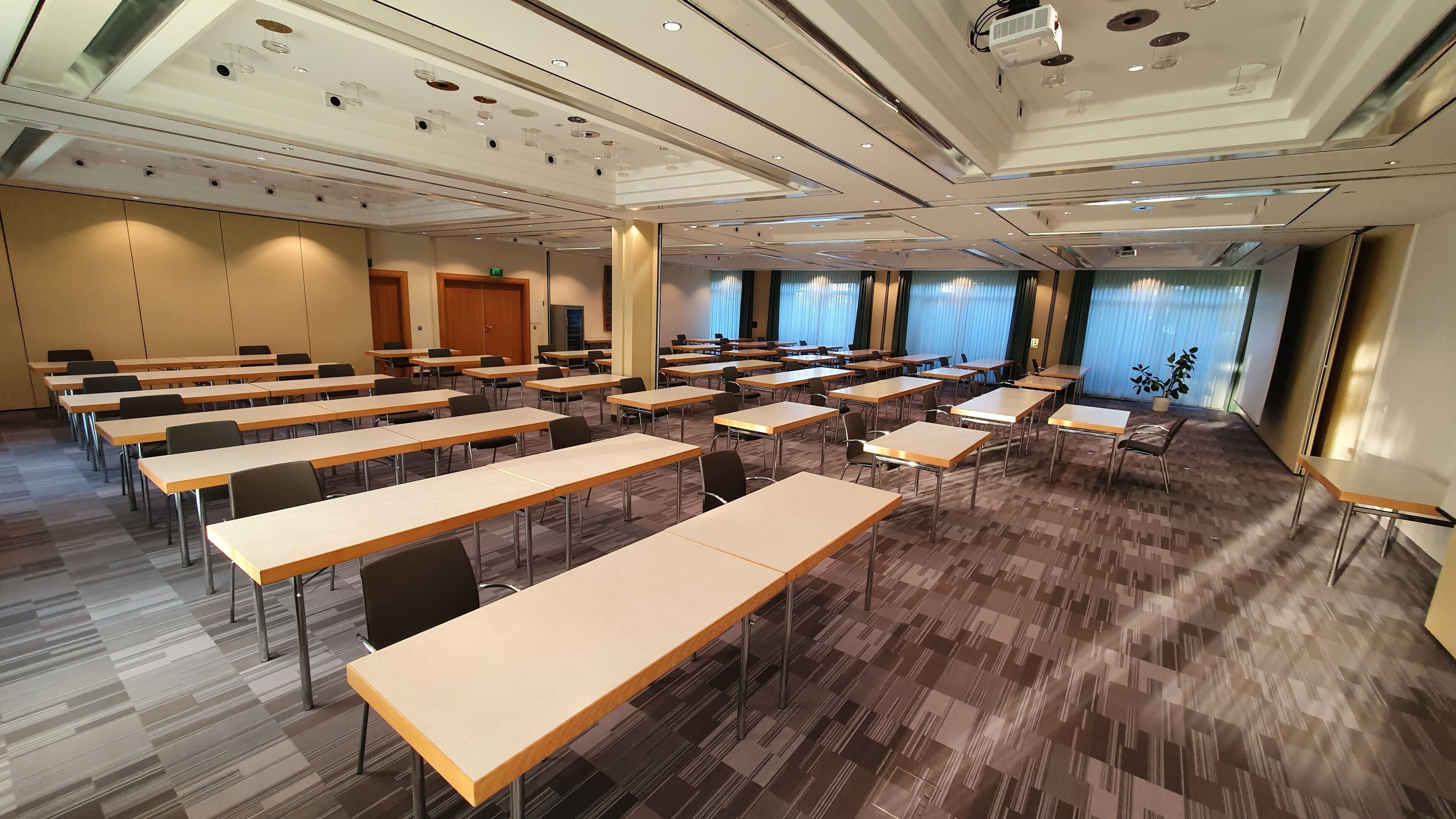 A conference room with multiple tables and chairs, large windows with blinds, and a modern ceiling design.