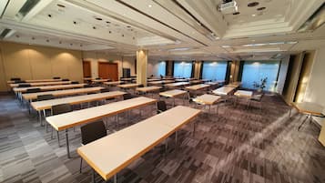 A conference room with multiple tables and chairs, large windows with blinds, and a modern ceiling design.