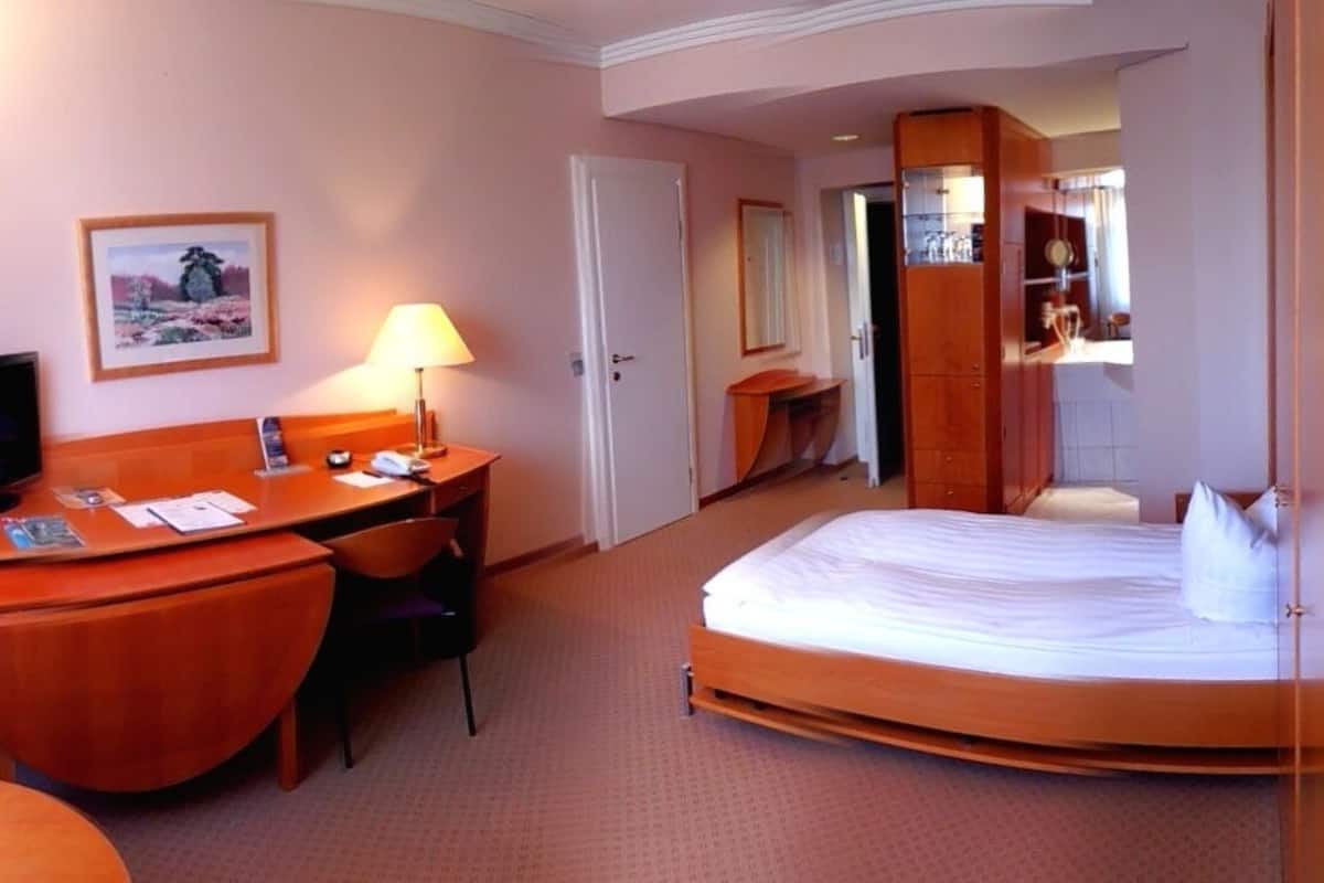 Una habitación de hotel con cama, escritorio, silla, televisión y espejo.