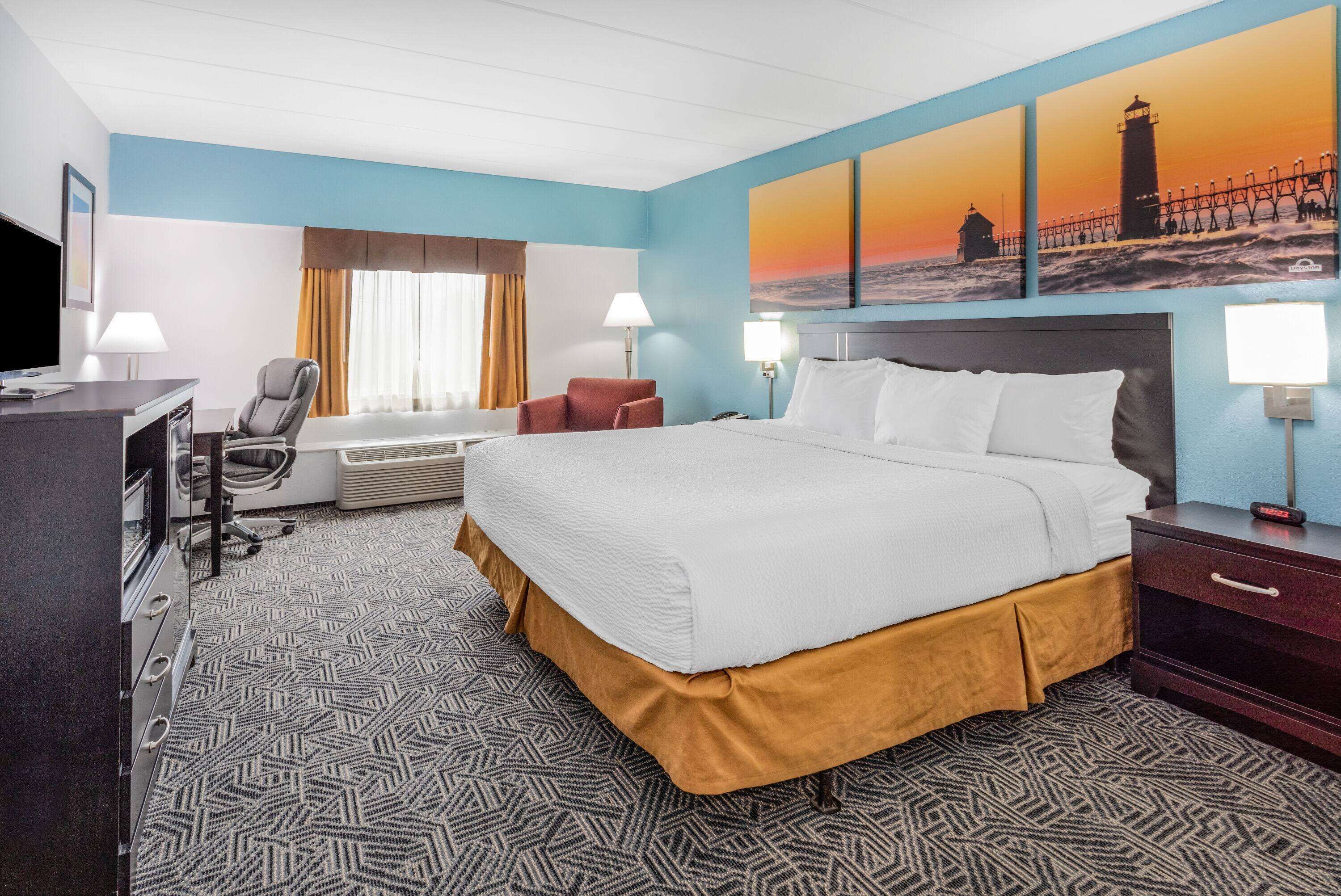 A hotel room with a large bed, a desk with a computer, a chair, and a TV.