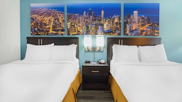 Une chambre d’hôtel avec deux lits, une table de chevet avec une lampe et un tableau représentant un paysage urbain accroché au mur.