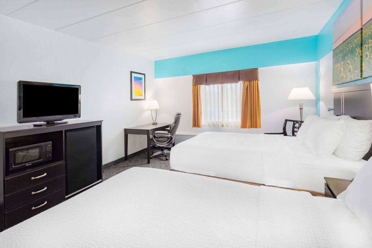 A hotel room with a bed, a desk, a chair, a television, and a window with curtains.