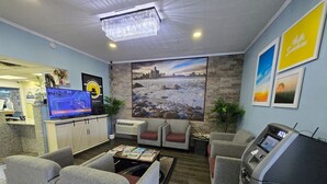 Un hall d’hôtel comprenant un comptoir d’accueil, un téléviseur à écran plat, un espace salon et un distributeur automatique de billets.