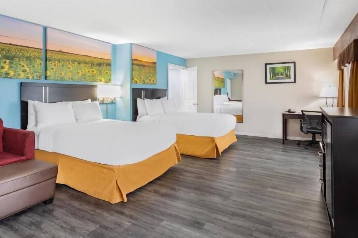 A hotel room with two beds, a desk, a TV, and artwork on the walls.