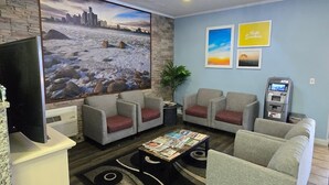 Un hall d’entrée agrémenté d’une grande fresque représentant un paysage urbain, doté de sièges confortables, d’une petite table avec des magazines et d’un distributeur automatique de billets.