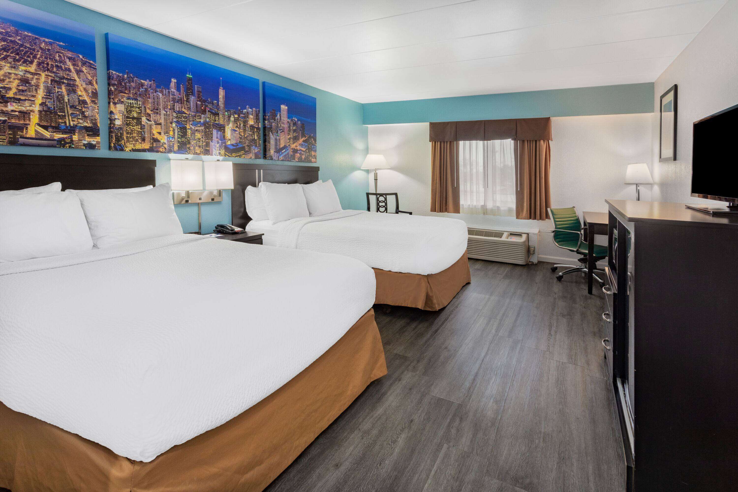 A hotel room with two beds, a desk, a television, and a cityscape mural on the wall.