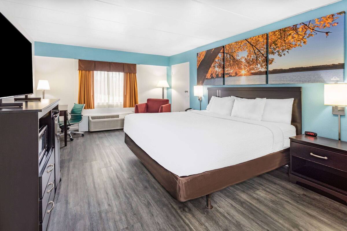 A hotel room with a large bed, a desk with a computer, a chair, and a TV.