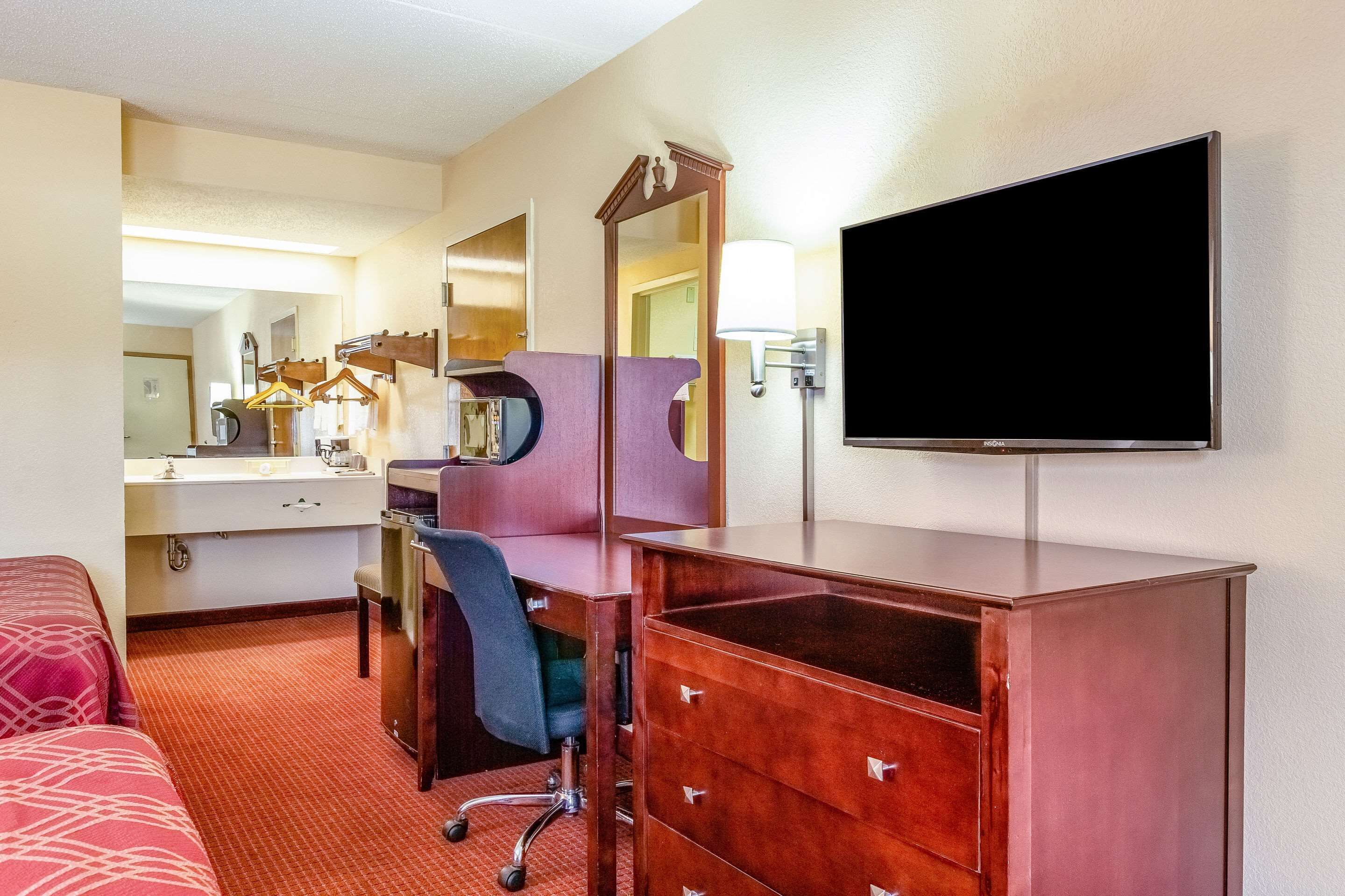 Habitación de hotel con cama, escritorio, silla, cómoda, espejo y televisión.