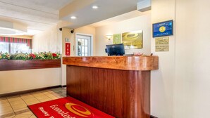 A hotel reception area with a wooden reception desk, a red carpet with the hotel logo, and a digital screen displaying room rates. - Econo Lodge Rocky Top (Rocky Top)