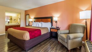 A hotel room with a large bed, a chair, a nightstand with a lamp, and a mirror. - Econo Lodge Rocky Top (Rocky Top)