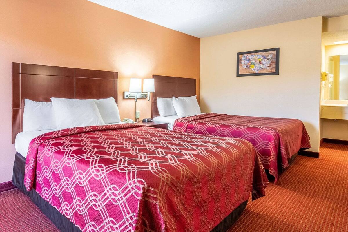 A hotel room with two beds, a nightstand, a lamp, and a framed picture on the wall.