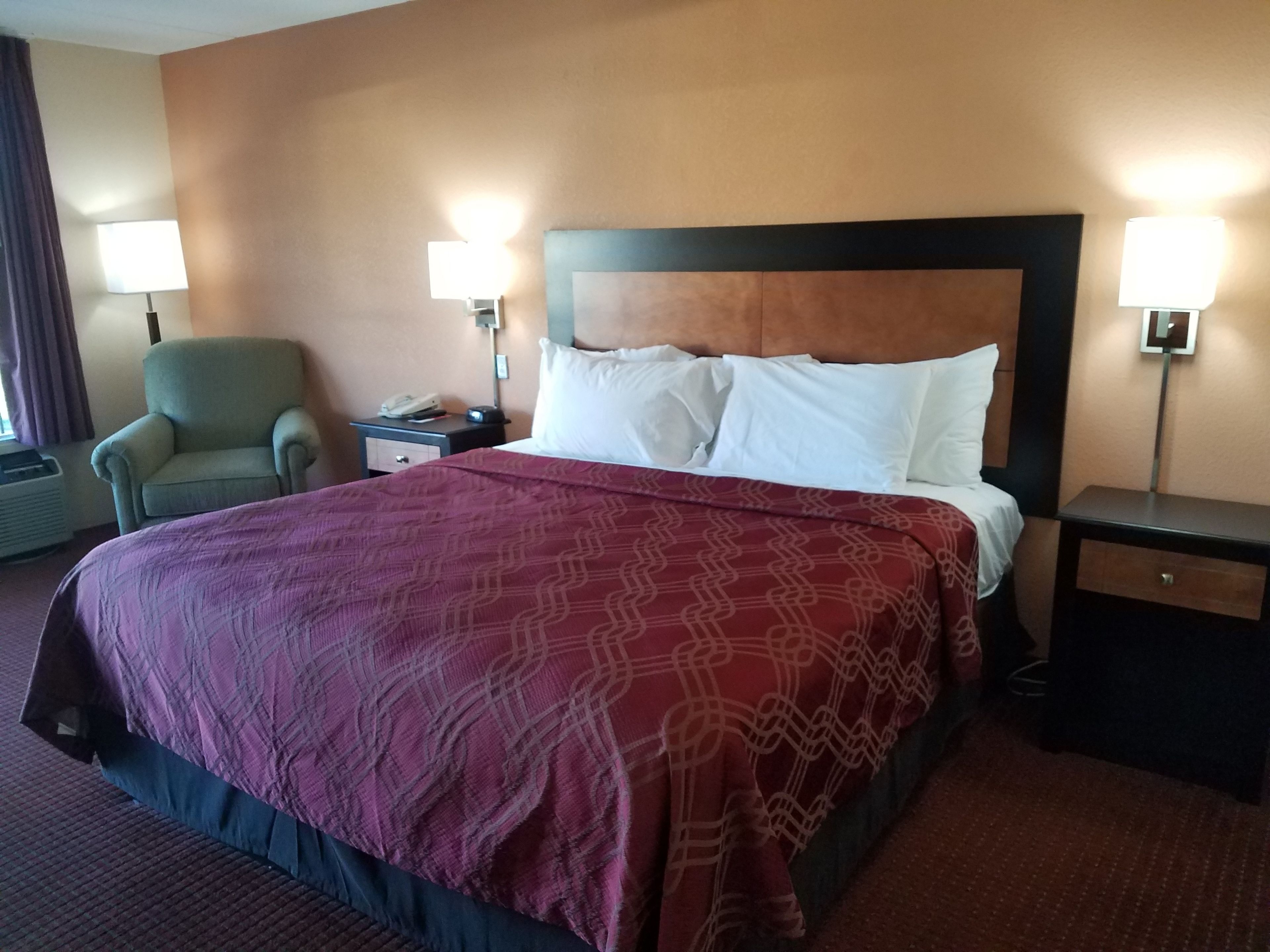 Una habitación de hotel con una cama grande, dos mesitas de noche, una silla y dos lámparas de pared.