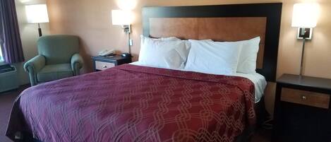 Una habitación de hotel con una cama grande, dos mesitas de noche, una silla y dos lámparas de pared.