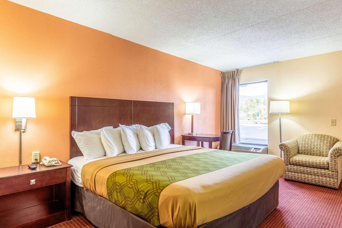 Habitación de hotel con una cama grande, dos mesitas de noche, una silla y una ventana con cortinas.
