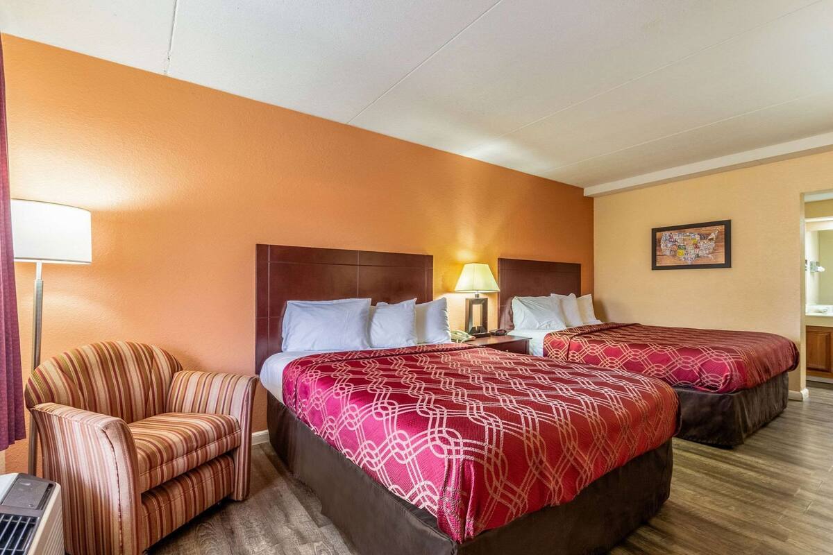 A hotel room with two beds, a chair, a lamp, and a map on the wall.