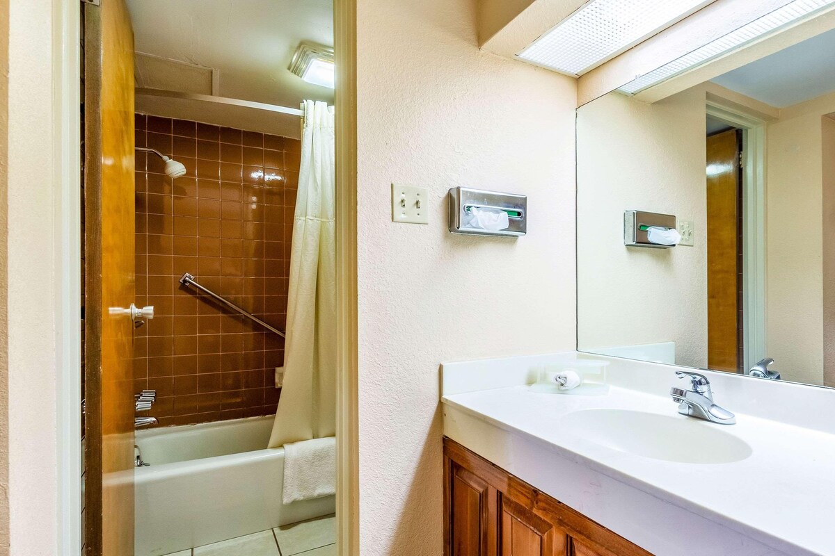 Un baño con bañera, lavamanos y espejo. Hay toalleros y una cortina de ducha.