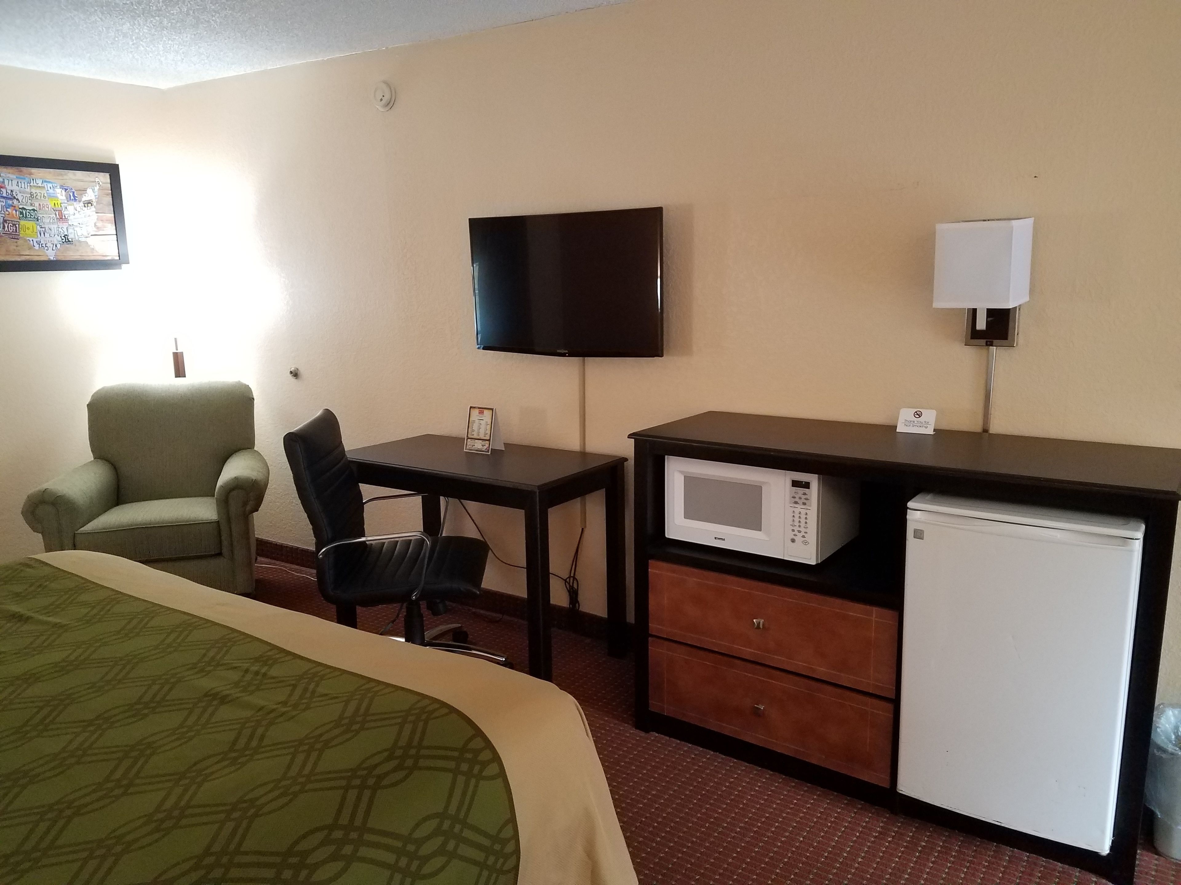 A hotel room with a bed, a desk with a chair, a television, a microwave, and a refrigerator.