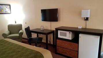 A hotel room with a bed, a desk with a chair, a television, a microwave, and a refrigerator.