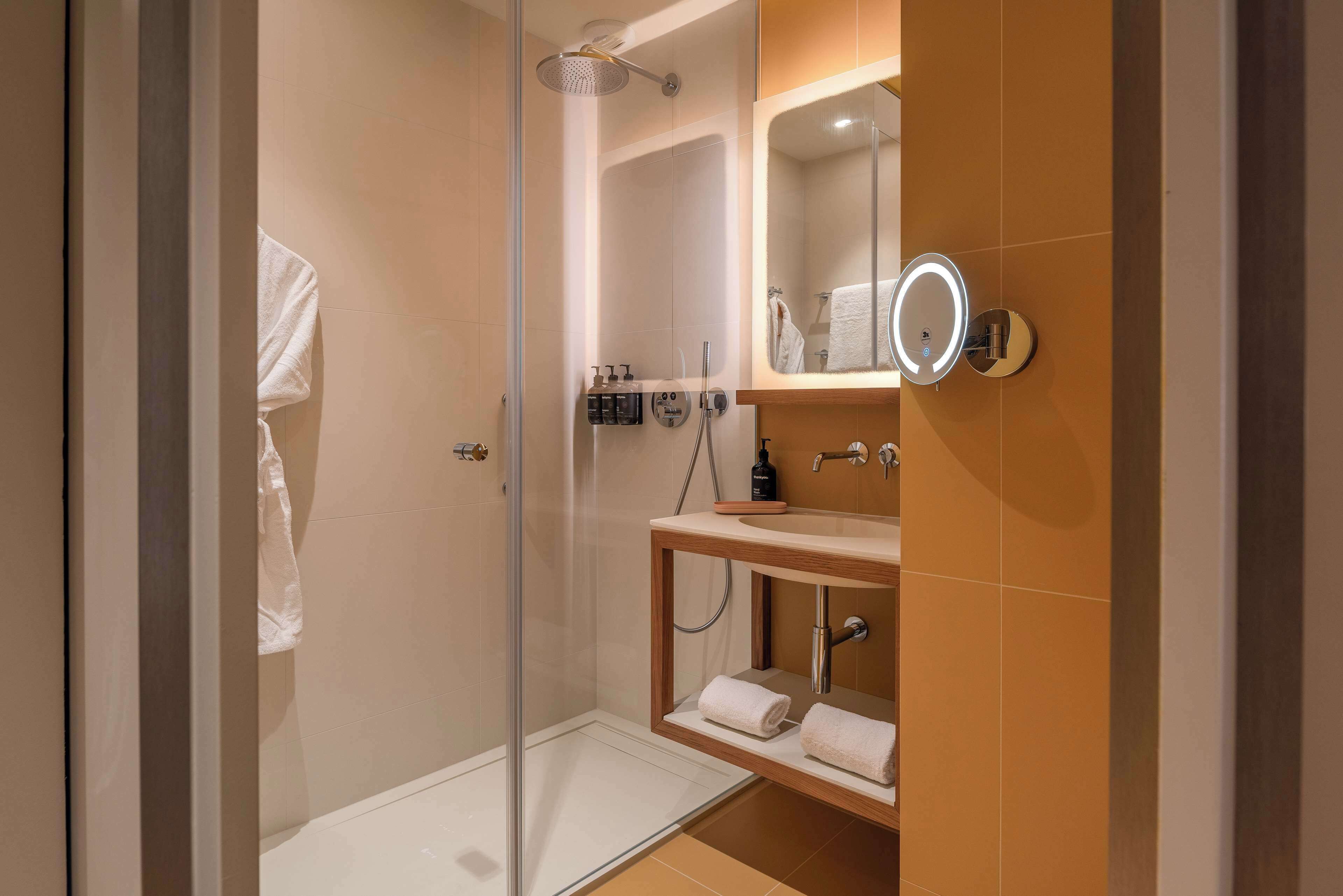 A modern bathroom with a glass-enclosed shower, a wooden vanity with a mirror, and a towel rack.