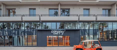 Ein modernes Gebäude mit einer Schaufensterfront mit der Aufschrift "canopy by Hilton" und einem roten Fahrzeug davor.