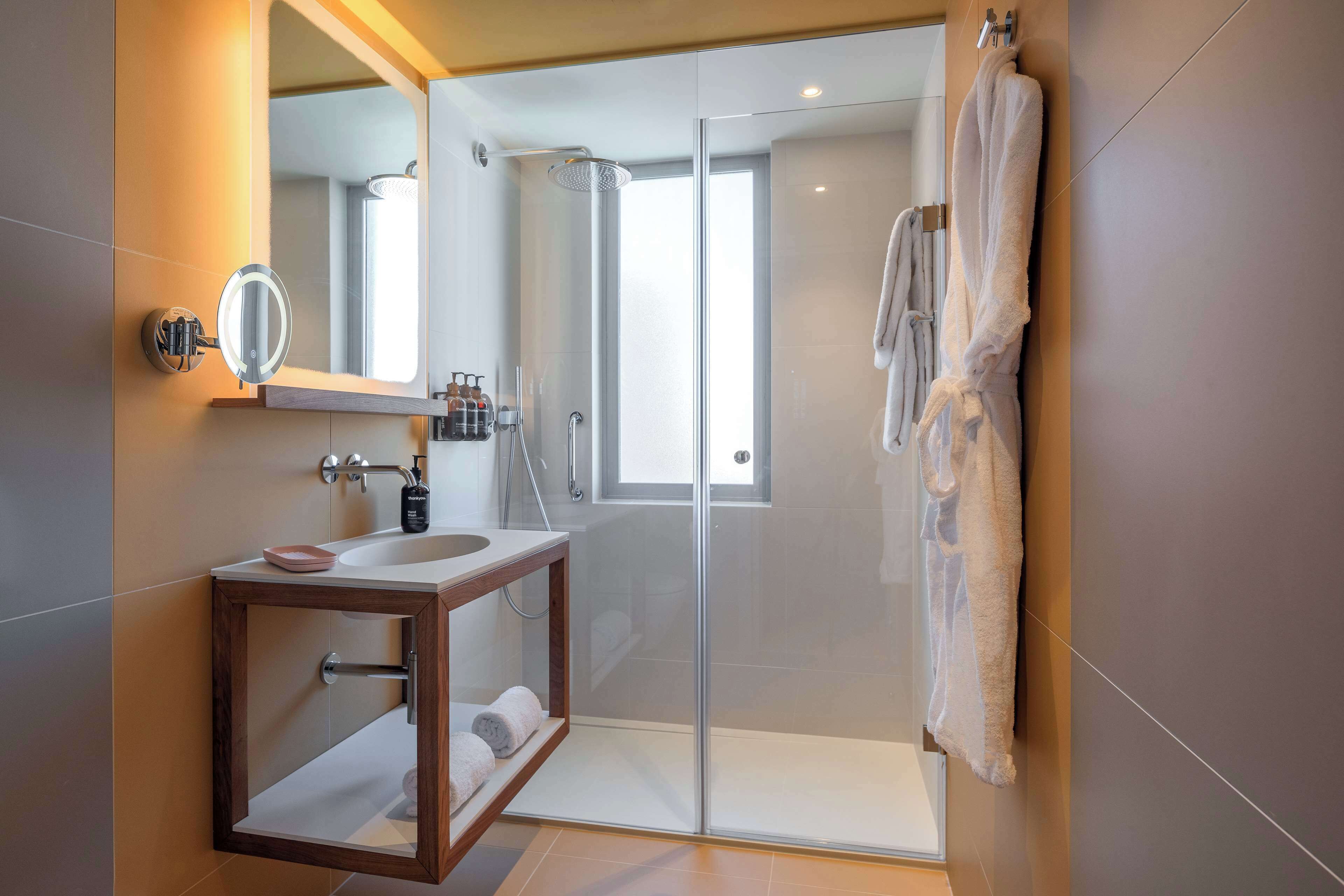 A modern bathroom with a glass shower enclosure, a wooden vanity, a large mirror, and a towel rack.