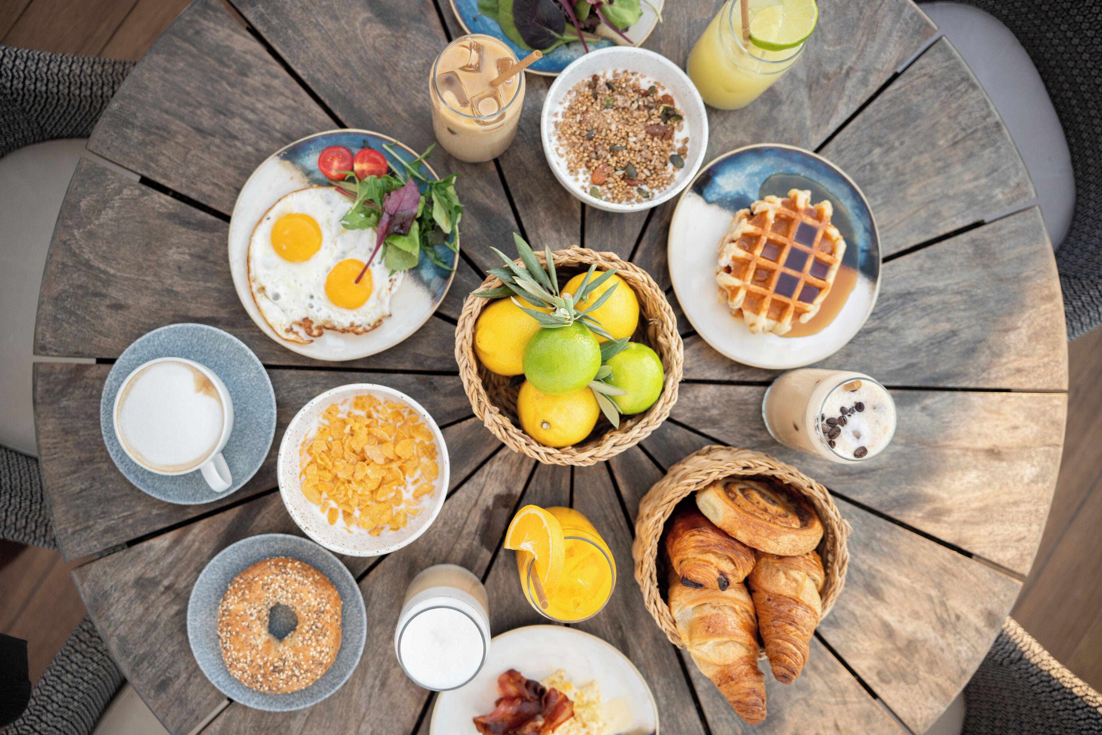 A round wooden table with breakfast items including eggs, croissants, and juice.