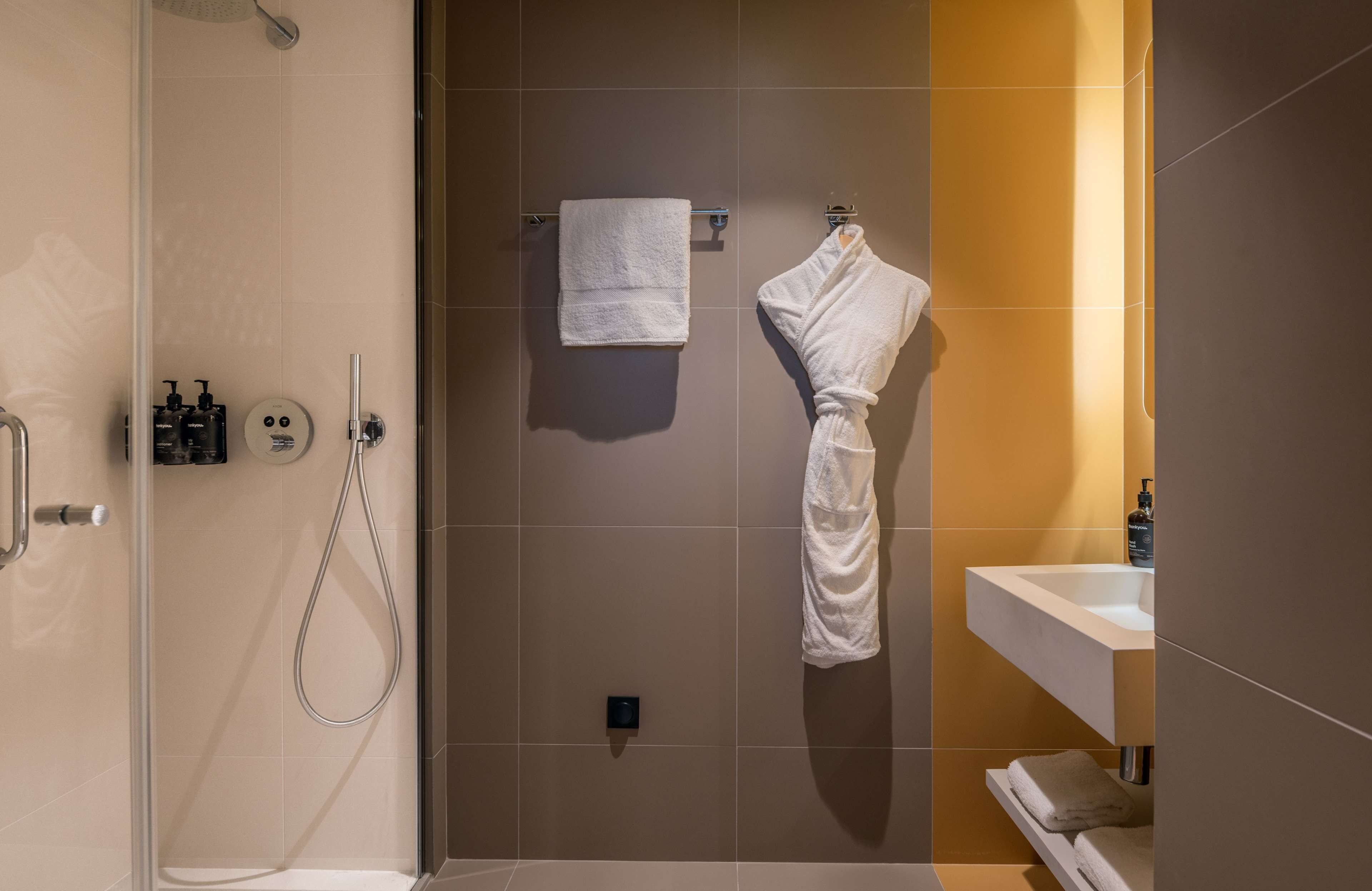 A modern bathroom with a glass-enclosed shower, a white towel, and a robe hanging on a rack.