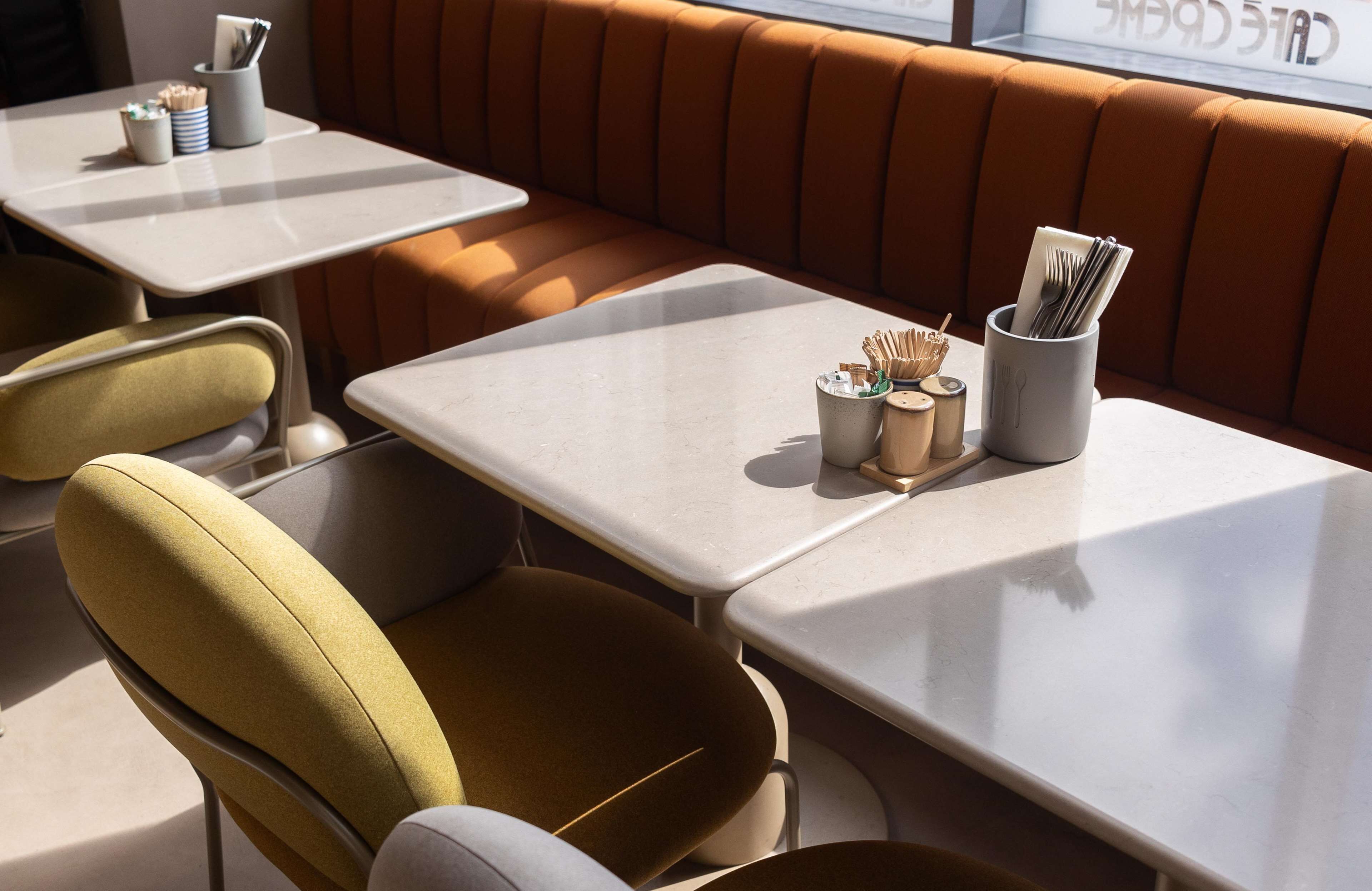 Interior de restaurante con cabinas y mesas, cada una con un porta vasos que contiene cubiertos y servilletas.