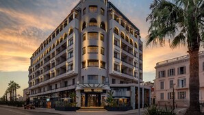 A multi-story hotel with a curved facade, multiple balconies, and a ground-level restaurant. - Canopy by Hilton Cannes (Cannes)