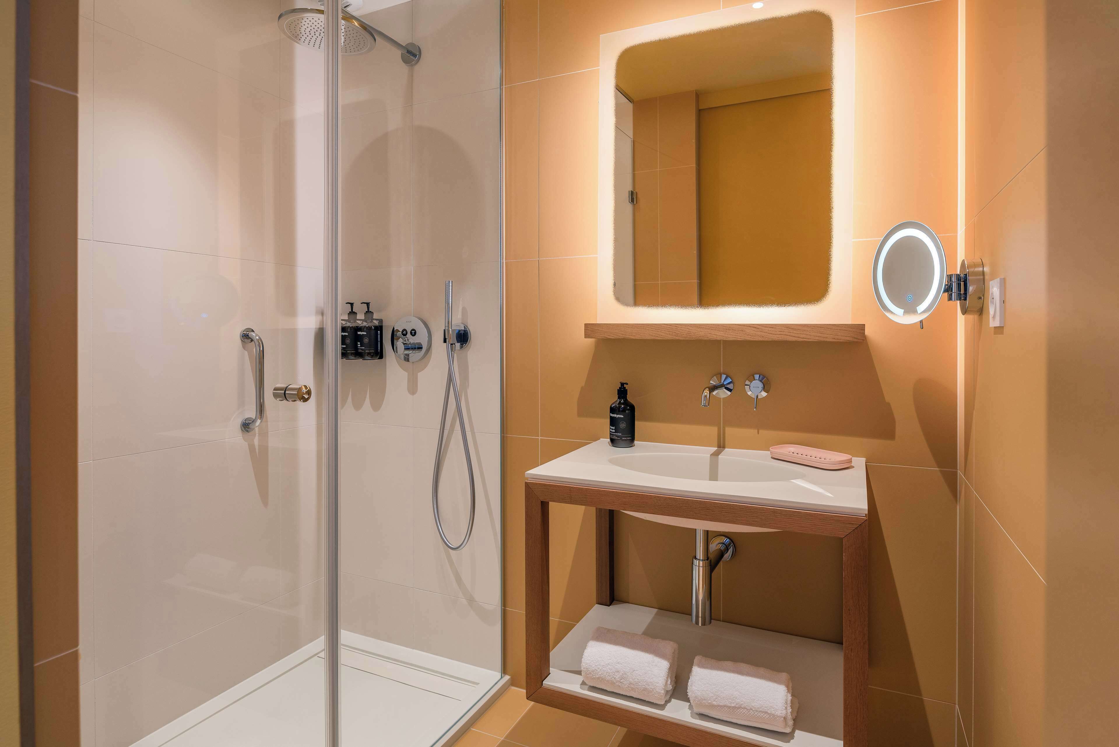 Een moderne badkamer met een douchecabine van glas, een houten wastafelmeubel met een spiegel, en twee handdoeken op de plank.
