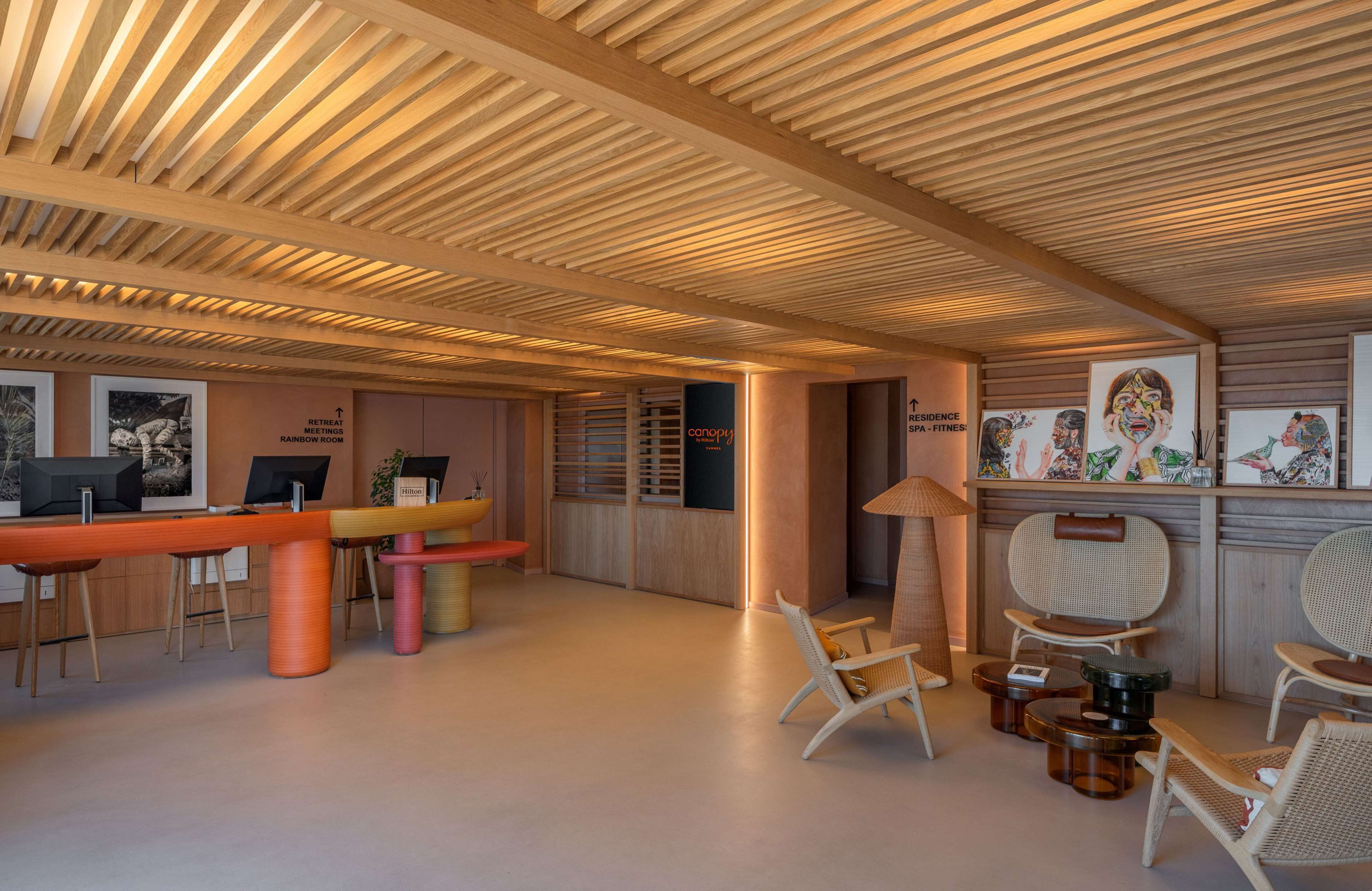 Un interno moderno con travi in legno a vista, una reception, poltrone e opere d'arte alle pareti.