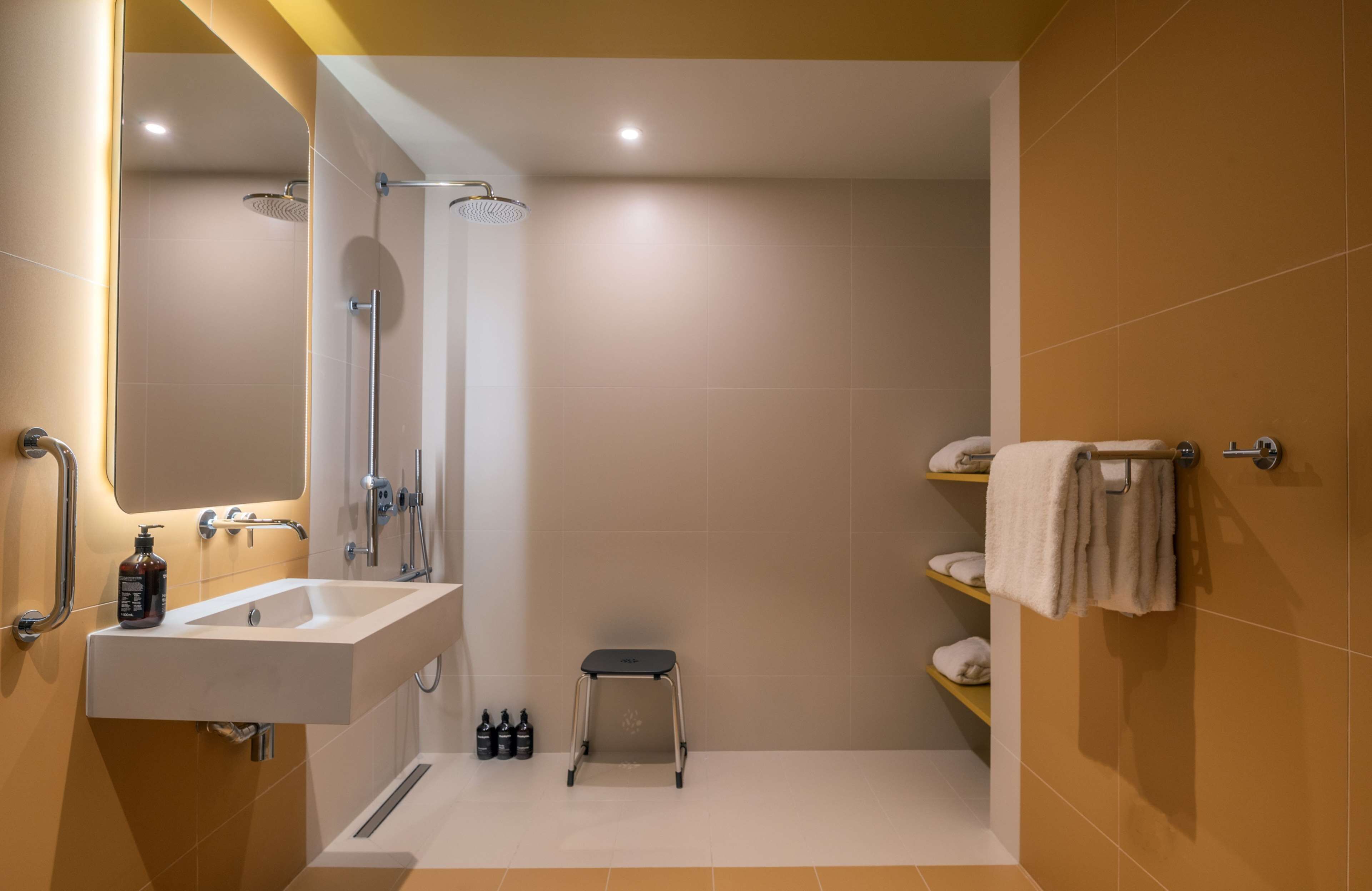 Un baño moderno con lavamanos, espejo, ducha y toallero.
