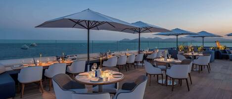 Une terrasse avec des tables et des chaises, donnant sur la mer.